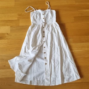 Vit klänning från H&M - En vit klänning från H&M i storlek 36 (S). Klänningen är ärmlös med smala axelband och har knappar framtill. Den är tillverkad i en linneblandning och har en smockad rygg för bättre passform.