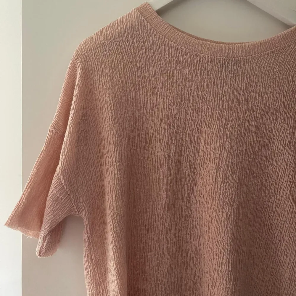 En ljusrosa tröja med korta ärmar och en rund halsringning. Tröjan har en lös passform och är tillverkad i ett texturerat material. 🌸💗✨. Neuletakit & Villapaidat.