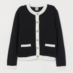 Svart kofta från Vero Moda - En elegant svart kofta från Vero Moda med vita detaljer. Koftan har långa ärmar, knappar framtill och två fickor. Den är perfekt för både vardag och fest.