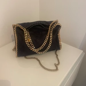 Stella Mccartney väska - Säljer denna Stella Mccarntey väska i mörkblå och guld. Den är jättesnygg samt i bra skick. Priset är väldigt bra pga har inte kvar äktshetbevis. Har köpt den själv för egna pengar så den är 100% äkta (kan man även se på insidan samt berlocken)💗💗