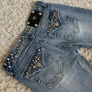 Vintage Miss Me jeans - Ljusblåa Miss Me jeans i lågmidjad och bootcut modell med snygga detaljer runt om midja och fickor. 🤍 Innerben: 81cm, midja rakt över: 35cm. 🐚 Har små defekter, därav priset. Meddela för bilder. 🫶
