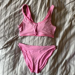 Rosa bikini från Weekday - En rosa bikini från Weekday där underdelen är storlek M och överdelen storlek L. Bikinin består av en topp med breda axelband och en matchande underdel. Dragkedja på överdelen. Materialet är mjukt och bekvämt, perfekt för sommarens bad och sol. ☀️ Väldigt bra kvalitet, har använts endast ett fåtal gånger.