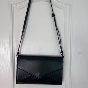 Svart handväska  - Ganska liten svart handväska. Långt justerbart band. Tofsen på sidan går att ta av😊