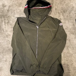 Moncler vindjacka grön - Moncler vindjacka i storlek två jackan är i bra skick men det finns ett hål i vänstra ficka