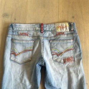 Ljusblåa lågmidjade jeans  - Superfina ljusblå lågmidjade jeans med coola mönster på fickorna! Jag har lagt ner de längst ner för att göra de längre, men annars är de i princip i nyskick. Midjemått: 80 cm, innerbenslängd: 72 cm. Skriv om du har några frågor!🫶