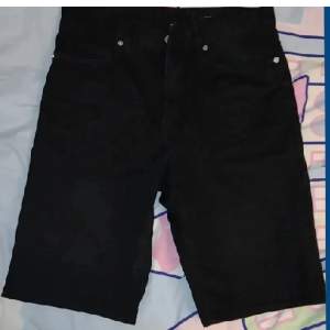 Svarta jeansshorts som slutar ovanför knäskålen. Passar både killar och tjejer. Riktiga fickor bak och fram, slim fit, silverimiterade knappar samt blixtlås. Storlek 29 (rekommenderar om du har xs på byxor och mindre höfter). Skriv vid frågor! 🥰