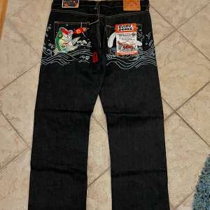 Evisu Genes jeans - Hejsan! Säljer nu dessa helt nya Evisu jeans då de är förstora för mig, har endast testat dem en gång. De är mörkblå/svarta i färgen. Mått: midjemått 48cm, ytterbenslängd 117cm, benöppning 24cm. Skriv vid frågor!