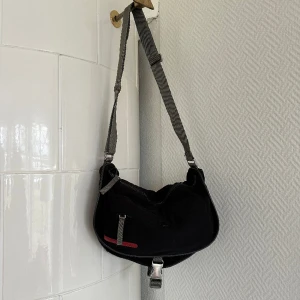 Prada Sports Bag - Prada Sports Bag i nylon, köpt på Humana i Malmö i våras. En mycket praktisk väska med justerbar rem och många fack. Det finns tecken på användning, men i övrigt är väskan i fint skick! DM för fler bilder, måtten är W35cm x H24cm x D1cm 🫶