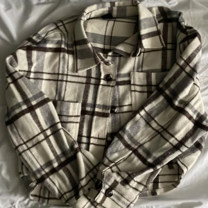 Tunn jacka - En fin tunn vår jacka i fina vår/höst färger. Den har bruna, gråa linjer med beige bakgrundu