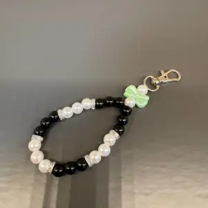 Egentillverkad nyckelring i svarta o vita pärlor och med söt liten rosett i grönt och en karbinhake som avslut. Är totalt 13 cm långt och med en omkrets på ca 14 cm.