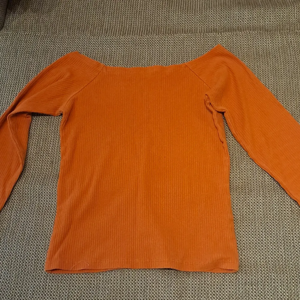 Säljer en snygg orange ribbad off-shoulder topp. Perfekt för vardag. Toppen är i ett mjukt och stretchigt material som sitter bekvämt på kroppen. Den har långa ärmar och en tight passform som framhäver figuren. Passar perfekt till höst- och vårsäsongen.. Toppar.