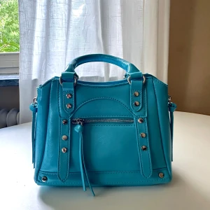 Handväska - Jag säljer en liten och söt handväska i en fin ljusblå färg! 💙 Medföljer extra axelremsband som man lätt kan ta på och av. (Aldrig använt)