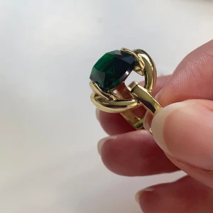 Guldfärgad ring med grön sten - Säljer en snygg guldfärgad ring med en stor, grön sten i mitten. Ringen har en unik design med en kedjeliknande struktur som håller stenen på plats. Perfekt för att ge en touch av elegans till din outfit! guldpläterad. stämplat 925 silver. justerbar 