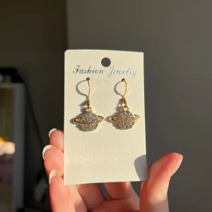 Guldörhängen med planetdesign - Säljer ett par snygga guldörhängen med en cool planetdesign. De är dekorerade med glittriga stenar som ger en extra touch av glamour. Perfekta för att piffa upp vilken outfit som helst! Säljes oanvända då jag är en silvertjej!🌟