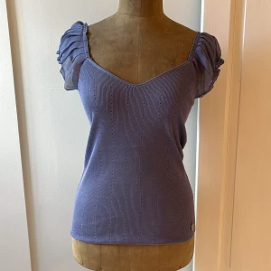 Blå topp från Guess by Marciano - Säljer en jättesöt blå/lila topp från Guess by Marciano. Den är ribbad och med v-ringad hals fram och bak. Rynkade ärmar i chiffong gör den extra fin. Perfekt för både vardag och fest! 