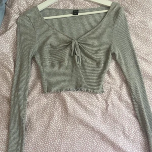 Grå ribbad topp från Shein - Säljer en superfin grå ribbad topp från Shein i storlek S. Toppen har långa ärmar och en söt knytning framtill. . Materialet är mjukt och stretchigt, vilket gör den bekväm att bära. använd flera gånger men har inga stora tecken på det