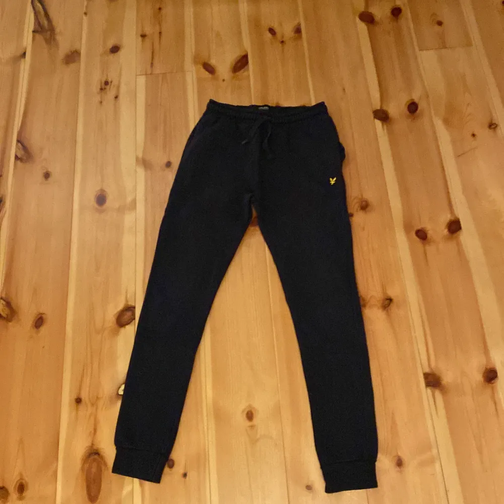 Säljer ett par svarta mjukisbyxor från Lyle & Scott i storlek 12/13 år. Byxorna har en elastisk midja med snörning och en liten gul logga på vänster sida. Perfekta för en avslappnad och bekväm stil. 🖤. Jeans & Byxor.