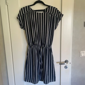 Svart och vit randig klänning - Säljer en superfin svart och vit randig klänning. Den är kortärmad och har en elastisk midja som ger en snygg passform. Klänningen är perfekt för både vardag och fest. Den är endast använd en gång, nyskick! 