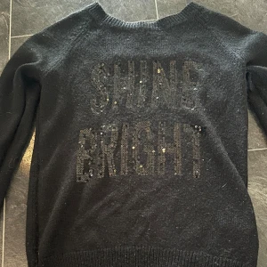 Svart stickad tröja från H&M - Säljer en svart stickad tröja från H&M med texten 'SHINE BRIGHT' i glittriga paljetter på framsidan. Tröjan har långa ärmar och är perfekt för höst och vinter. Den är i bra skick och supermysig att ha på sig. Perfekt för att lysa upp mörka dagar! ✨