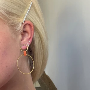 Guliga örhängen med orange sten - Runda örhängen med orange detalj, använda 1 gång. Köpta i paris på en ”no brand” butik. Inte äkta guld. Pris kan diskuteras vid snabb affär!