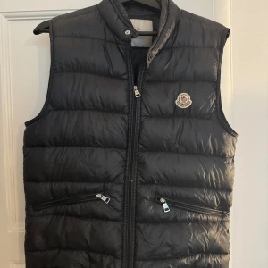 Moncler Gui Väst - Moncler Gui down väst köpt från Kaspersheat! Givetvis äkta men gammal model. Storlek 3 vilket motsvarar M/S  Skick 7/10 finns ett lagat hål (syns ej) och litet hål vid dragkedjan, finns fläckar.  Nypris ~8000kr Mitt pris 2349kr Frågor? Dm!