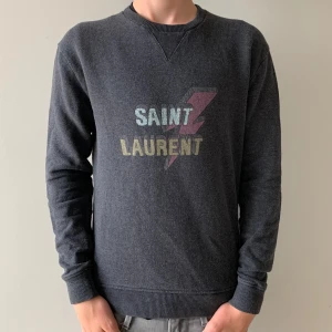 Saint Laurent Tröja - Äkta och extremt snygg ysl tröja i prima skick utom att lappen med loggan på åkt av eftersom (inte ovanligt med ysl tröjor överlag.) Kille i bild: 177 cm sitter nästan perfekt endast nån cm kort i längden. Tröjan är mörkgrå nästan svart. 
