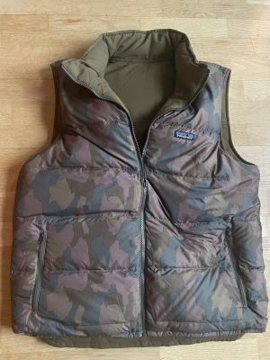Patagonia Reversible Bivy Down Vest - Jättteskön vändbar väst från Patagonia. På ena sidan militärgrön och på andra sidan kamouflage i samma färger.