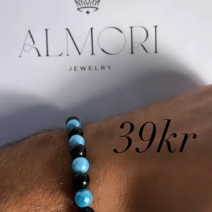 Armband från Almori Jewelry - Ett armband från Almori Jewelry med pärlor i blått och svart. Armbandet har en enkel och elegant design.