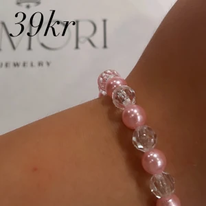 Rosa pärlarmband från Amori - Ett elegant armband från Amori med rosa pärlor och genomskinliga kristallpärlor. Armbandet är elastiskt och passar de flesta handleder.