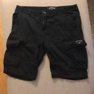 Ett par svarta shorts från Polo Club med flera fickor, inklusive sidofickor med lock. Shortsen har en knapp och dragkedja framtill.