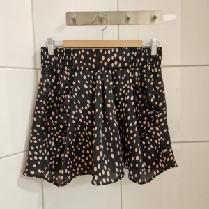 Y2K Kjol (Nyskick) Strl M - Kjol   Strl M Nyskick! Färg: Svart, Ljusrosa Twenty One  Kort vippig kjol i Y2K-stil. Prickigt mönster. Resår bak i midjan, fickor i sidorna. Sparsamt använd. Märkt strl L, men är liten i storleken.