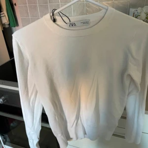 Vit långärmad tröja från Zara - En enkel och stilren vit långärmad tröja från Zara. Tröjan har en rund halsringning och knappar vid ärmsluten.