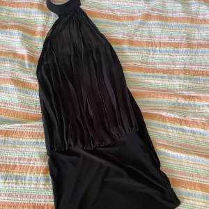 Svart klänning från DAY - En elegant svart klänning från DAY med en halterneck-design. Klänningen har en mesh del över bandeuklänningen 