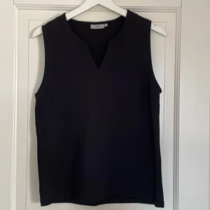 Svart ärmlös topp från Monki - En svart ärmlös topp från me&i med en enkel och stilren design. Toppen har en v-ringad hals och är tillverkad i ett mjukt och bekvämt material.