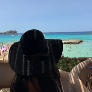 Svart solhatt - En elegant svart solhatt med bred brätte, perfekt för soliga dagar på stranden. Hatten har en dekorativ snörning runt basen av kullen med snäckor!