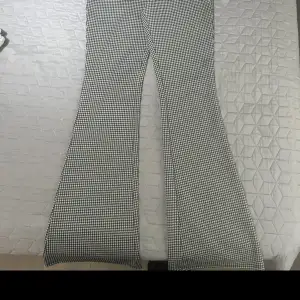 Ett par svartvita rutiga byxor med bootcut-stil. Byxorna har en hög midja och är tillverkade i ett bekvämt material.oanvänd 