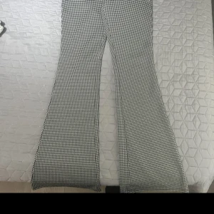 Svartvita rutiga byxor - Ett par svartvita rutiga byxor med bootcut-stil. Byxorna har en hög midja och är tillverkade i ett bekvämt material.oanvänd 