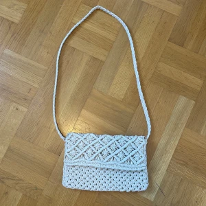 Beige stickad axelväska från Ellos - En beige stickad axelväska från Ellos med ett dekorativt mönster. Väskan har en lång axelrem och är fodrad på insidan. Det går också bra att ha väskan som en kort axelväska ❤️ Superbra skick