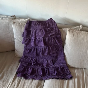 Lila kjol med volanger - En lila kjol med flera lager av volanger. Kjolen har en glittrig yta och vadlång. 