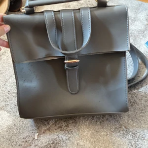 Väska -  En grå Väska med ganska bra plats för saker man kan ha den som en ryggsäck och en axelväska