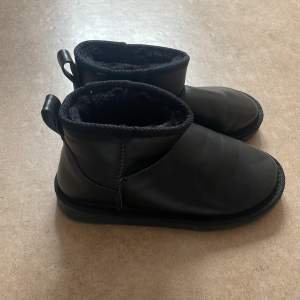 Ett par svarta boots med foder. Skorna har en rund tå och en dragflik baktill för enkel påtagning. Sulan har ett mönster för bättre grepp.