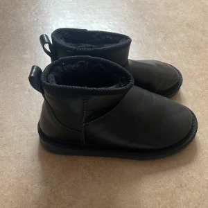 Svarta boots med foder - Ett par svarta boots med foder. Skorna har en rund tå och en dragflik baktill för enkel påtagning. Sulan har ett mönster för bättre grepp.