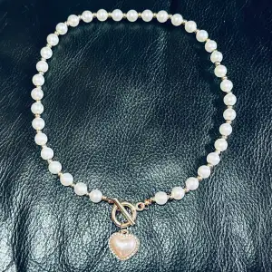 Nytt pärlhalsband / Pärlchoker med pärlhjärta. Pärlor med vacker lyster & glittrande strass. Pärlor är 6mm, halsbandet 45 cm långt. Faux pearls, mässing & strass. En fin gåva till dig själv eller någon du har nära hjärtat. Färdigprutat.