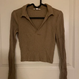 BEIGE TRÖJA - Beige, ribbad tröja med urringning och krage från H&M. Bra kvalitet och skick, den är lite skrynklig på bilden för att den varit ihopvikt men efter en tvätt så försvinner det. Storlek XS, köpt för 250kr, säljer nu för 150kr.