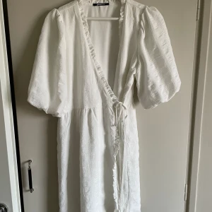 Vit klänning med ballongärm & krås  - En vit kort klänning med kort ballongärm, knyt i midjan och krås. Använd på midsommar förra året så klänningen är i nyskick.   