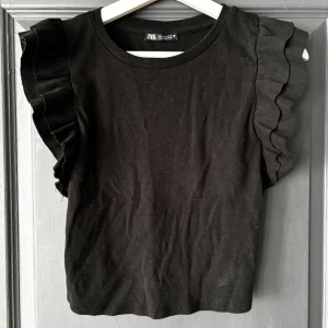 Svart volangtop  - Denna tröja är från Zara och är i storlek L men är liten i storleken så snarare en storlek M. Den är använd men fortfarande i bra skick. Det är en top som är kort i längden och sitter åt 