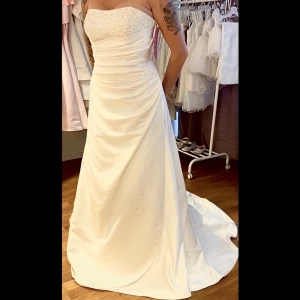 NY Bröllopsklänning  - Otroligt fin Brudklänning, stl. 44 (L).  Oanvänd, prislapp kvar.  satintyg från Gino Cerruti. Storlek Large men mer som en M/L   Pärlor längs med midjan.  Pärlor och paljetter vid/på bysten.  Inbyggda kupor. Överdrag 