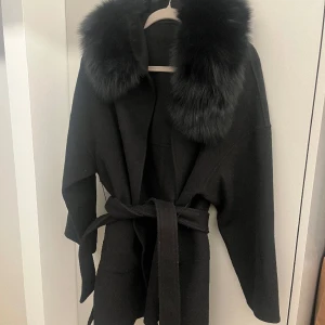 Ullkappa med päls  - Ullkappa med äkta päls på luvan. Använd fåtal gånger, värmer bra. Jackan är OVERSIZE så passar XS-S-M 