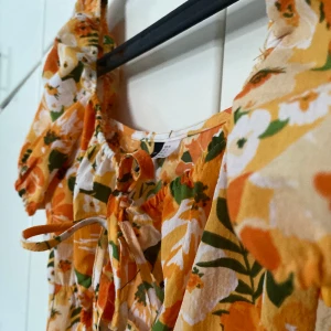 Somrig klänning - En orange-blommig som har ett öppetparti vid magen. (Inte jättestort) storlek 38 men jag tycker den är liten i storleken.