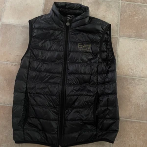 Ea7 väst  - En snygg och skön väst från ea7. Glansig svart med guldig logga! Jättefint skick då den är välanvänd, 9/10. Hör av dig vid frågor. Priset går att diskutera vid snabb affär!